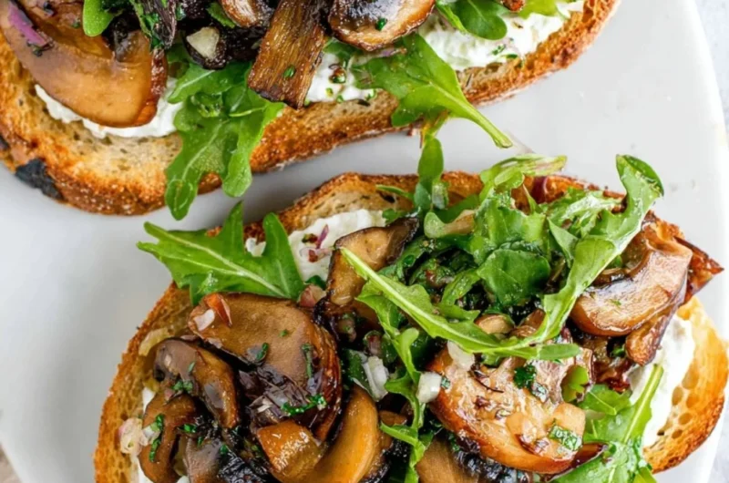 Creamy mushroom toast topped with herbs and spices, served on toasted bread.
