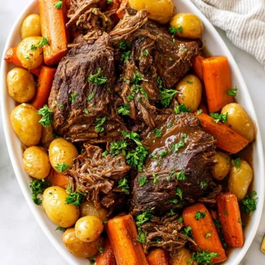 Crock pot pot roast with vegetables and gravy in a serving dish.