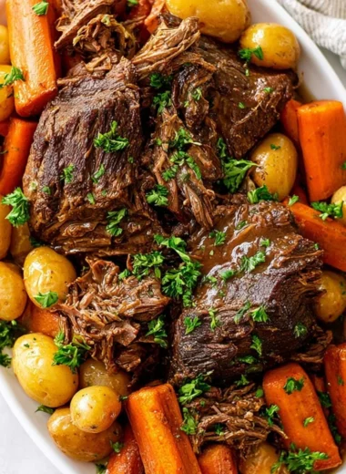 Crock pot pot roast with vegetables and gravy in a serving dish.
