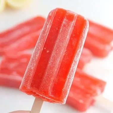 Strawberry lemonade popsicles on a wooden table with fresh strawberries and lemons.