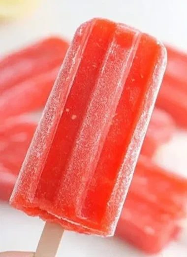 Strawberry lemonade popsicles on a wooden table with fresh strawberries and lemons.