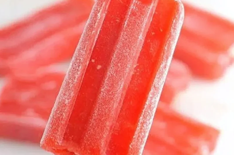 Strawberry lemonade popsicles on a wooden table with fresh strawberries and lemons.
