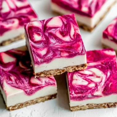 Vegan raspberry cheesecake bars topped with fresh raspberries on a wooden table