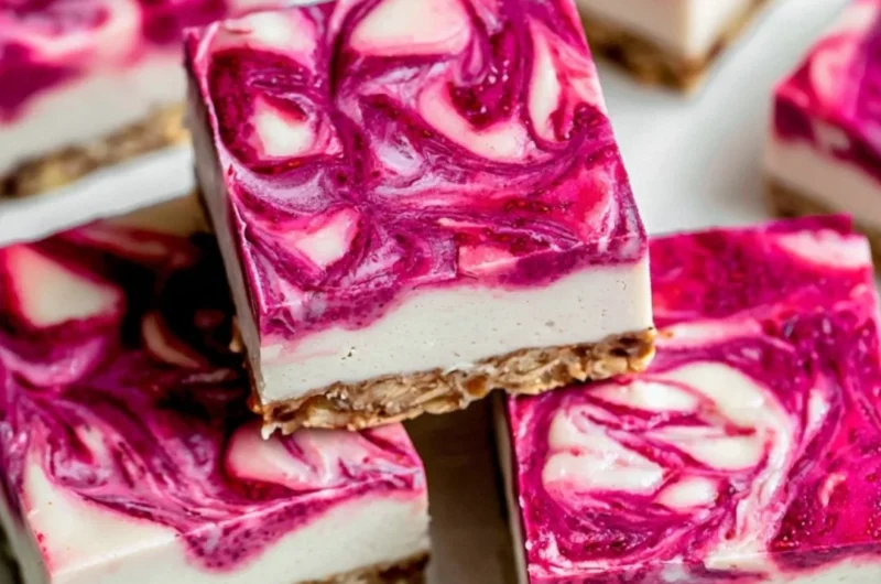 Vegan raspberry cheesecake bars topped with fresh raspberries on a wooden table