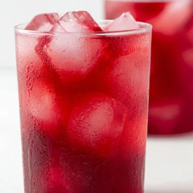 A refreshing glass of strawberry hibiscus iced tea with fresh berries and hibiscus flowers.