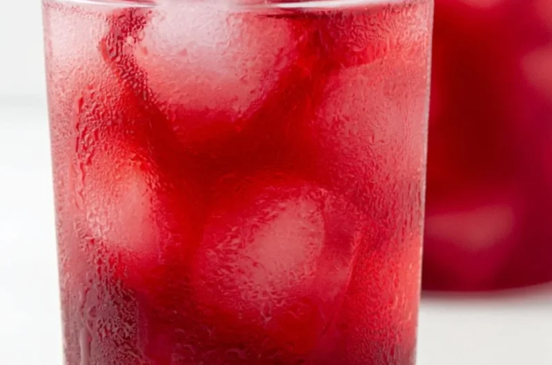 A refreshing glass of strawberry hibiscus iced tea with fresh berries and hibiscus flowers.