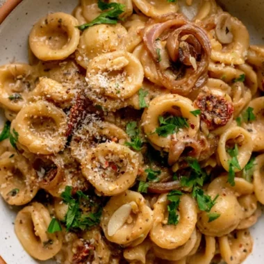 A bowl of creamy caramelized onion pasta topped with fresh herbs and parmesan cheese.