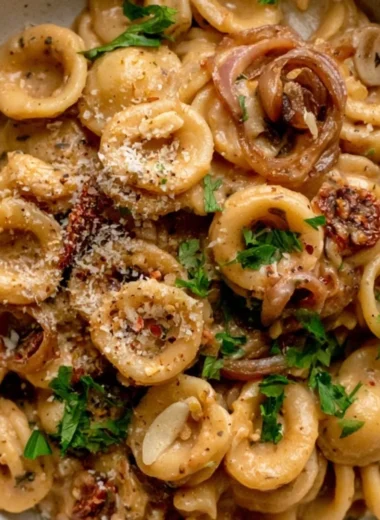 A bowl of creamy caramelized onion pasta topped with fresh herbs and parmesan cheese.