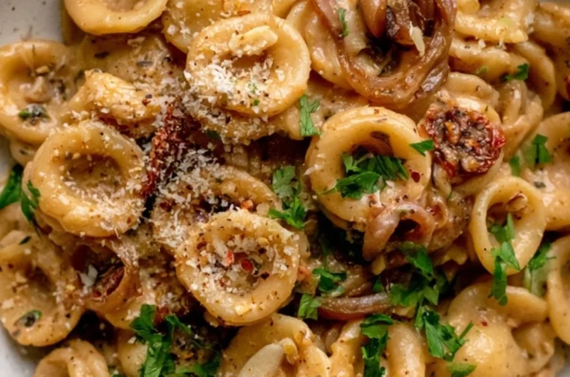 A bowl of creamy caramelized onion pasta topped with fresh herbs and parmesan cheese.